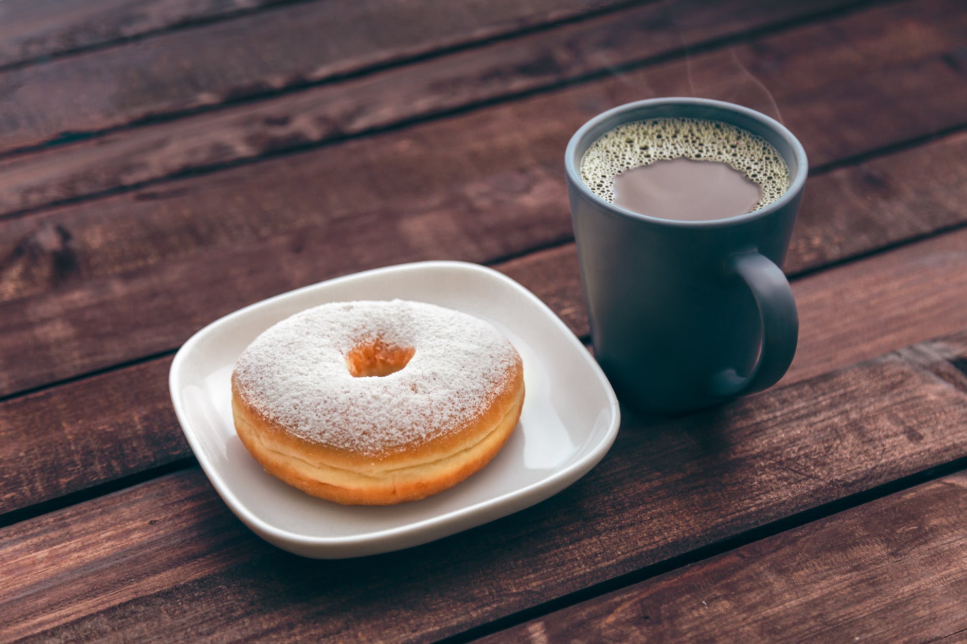 doughnut on white ceramic plate beside ceramic mug on brown wooden table